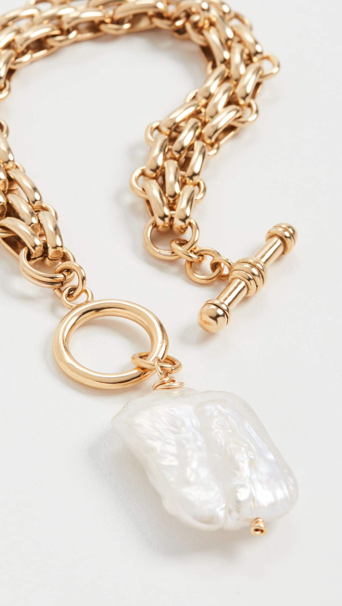Extreme close-up of the Brinker + Eliza Penny Bracelet highlighting the unique baroque pearl charm and toggle clasp.