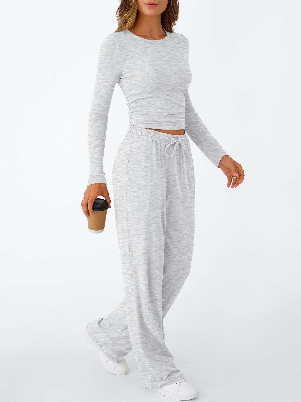 A woman styled in a chic grey 2-piece sweatsuit holding a coffee cup, representing effortless airport or travel fashion.